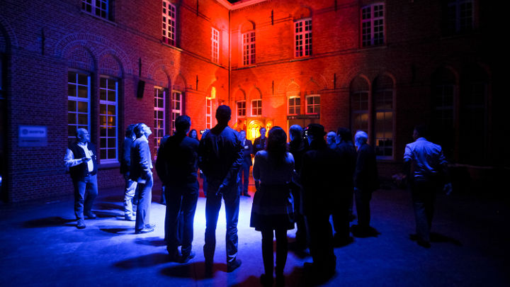 在由飞利浦组织的一场研讨会中，一大群人正站在比利时蒂伦豪特的一栋灯火璀璨的大楼前进行讨论
