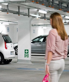 一位女士在采用 Green Parking 系统的明亮室内停车场中前去取车。- 商场照明