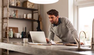 一名男子在照明良好的家庭办公室中使用笔记本电脑，并配有 LED 工作照明，以实现高效的远程工作环境。